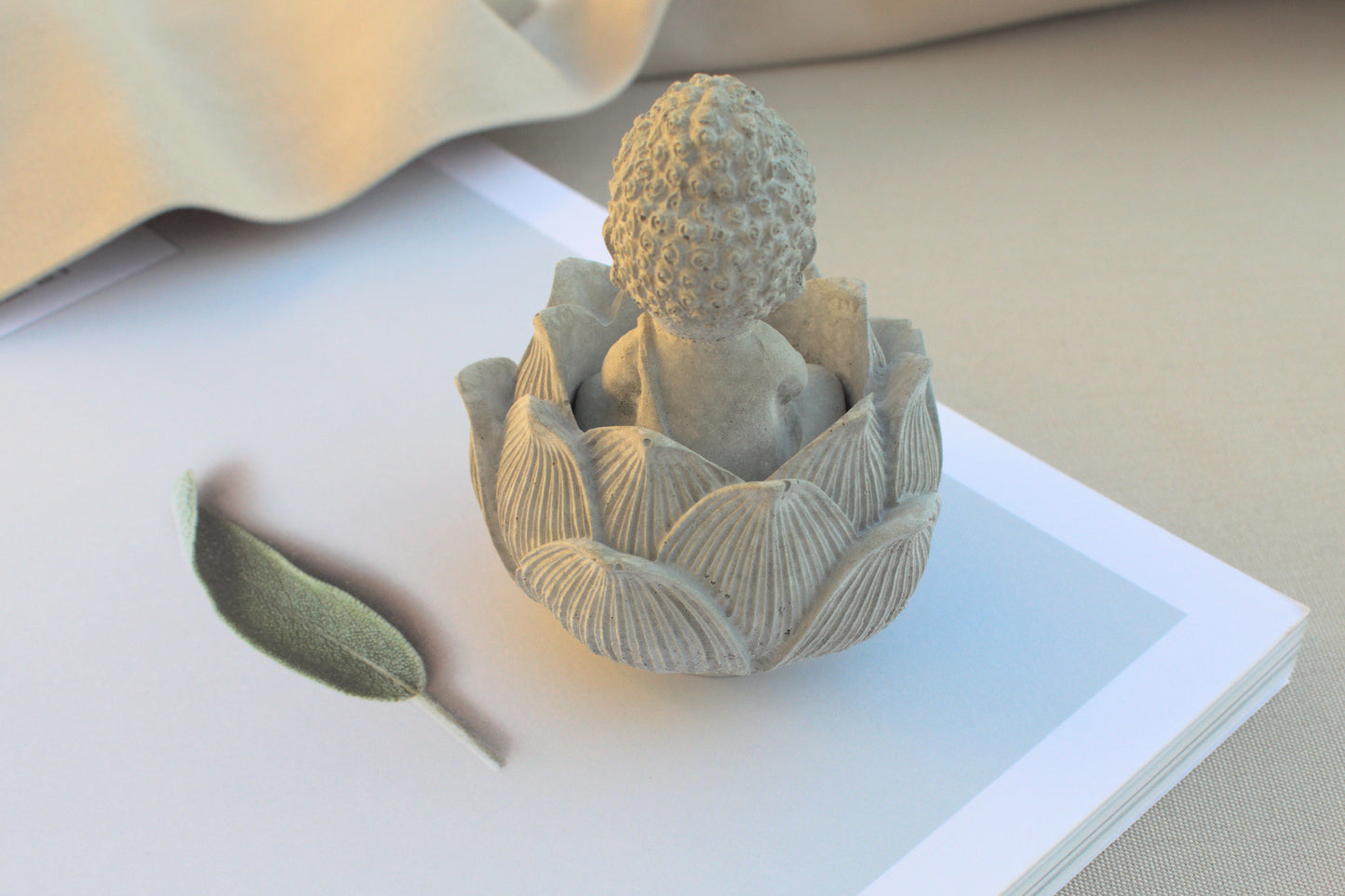 Kleiner Budda mit Lotusblüte aus grauem Beton für Ruhe beim Yoga